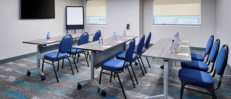 A conference room with a long table, blue chairs, a projector screen, and a whiteboard.