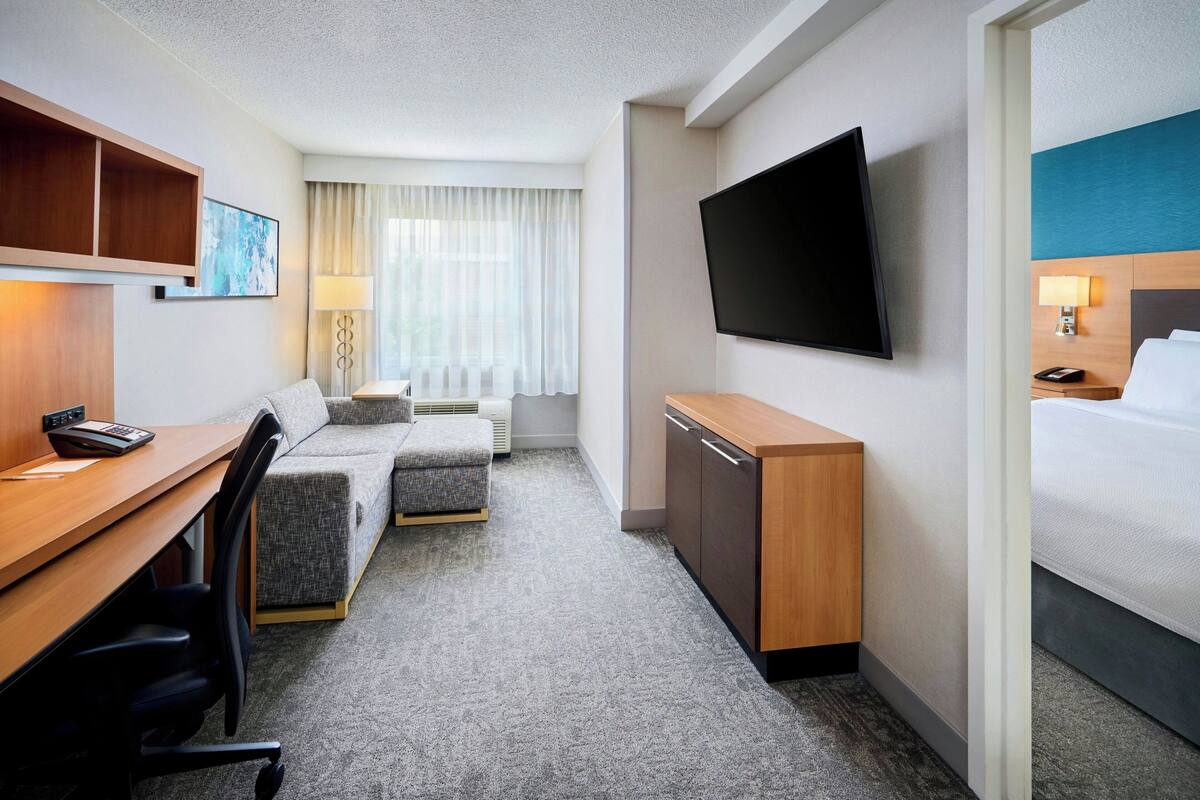 Une chambre d’hôtel équipée d’un bureau, de deux canapés, d’une télévision, d’un lit et d’un mini-bar.