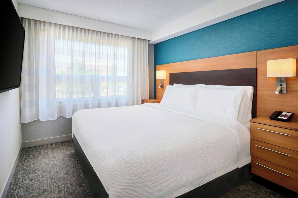Une chambre d’hôtel avec un grand lit, une table de chevet en bois avec une lampe et un téléphone.