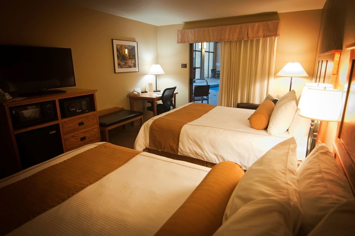 A hotel room with two beds, a desk, a television, and a view of the outdoors.