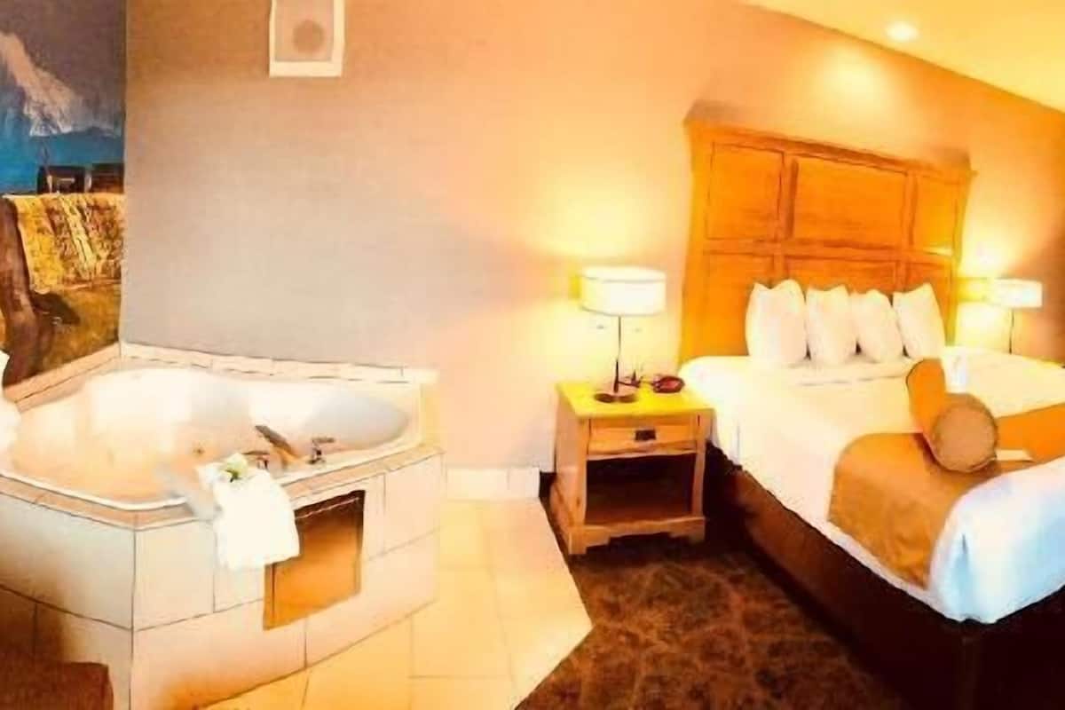 A hotel room with a large bed, a separate bathroom with a bathtub, and a view of a mountainous landscape.