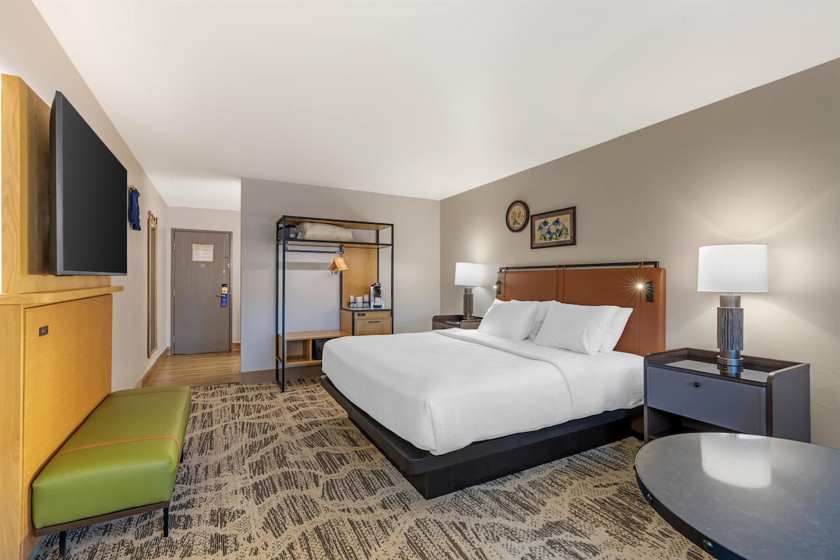 A hotel room with a bed, a desk, a chair, a TV, a door, and a small table.