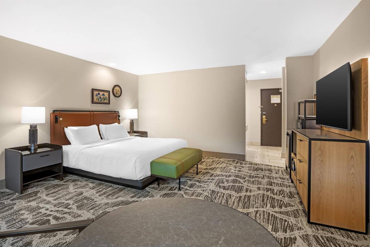 A hotel room with a bed, bedside tables, a bench, a TV, and a desk with drawers.