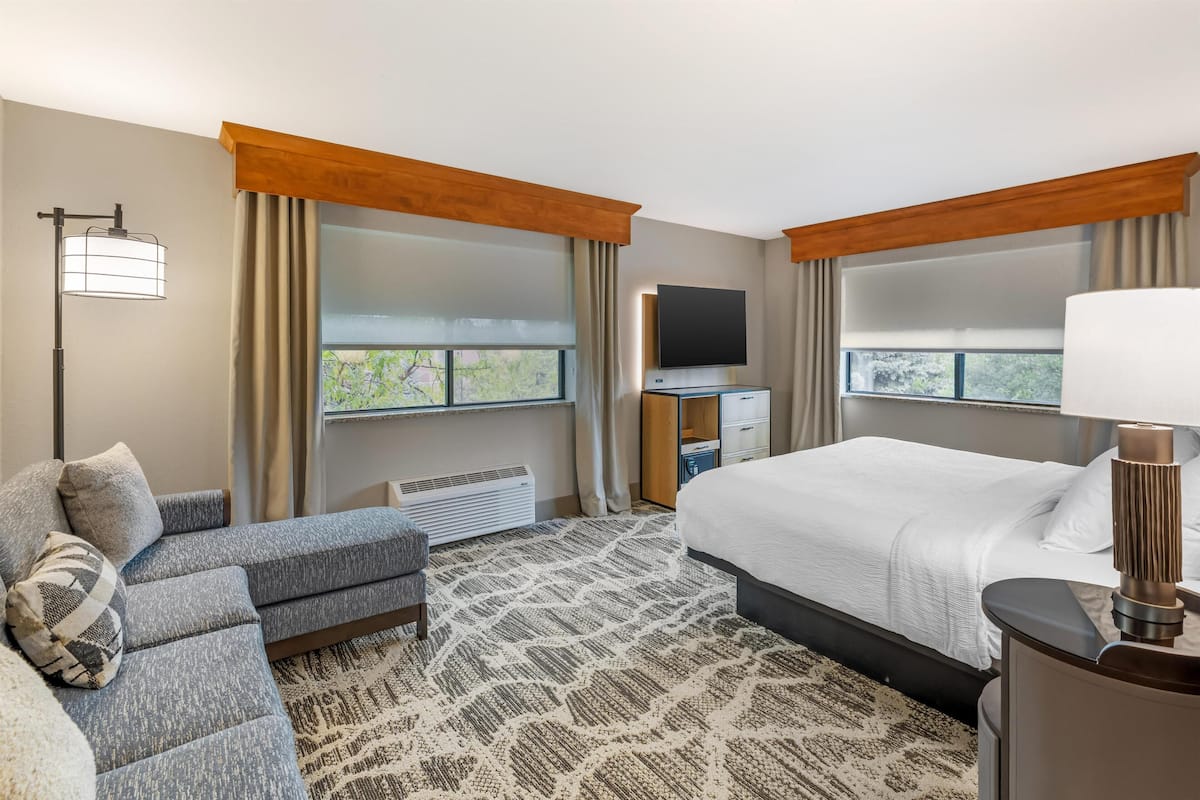 A hotel room with a bed, a sofa, a TV, a desk, and a window with curtains.