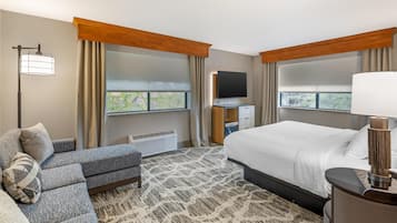 A hotel room with a bed, a sofa, a TV, a desk, and a window with curtains.