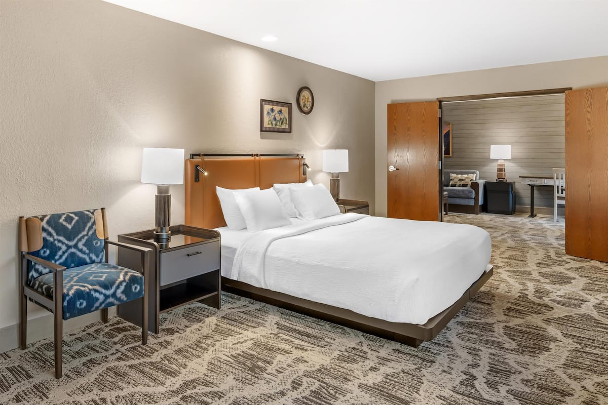 A hotel room with a bed, two bedside tables with lamps, a chair, a desk, and a wardrobe.