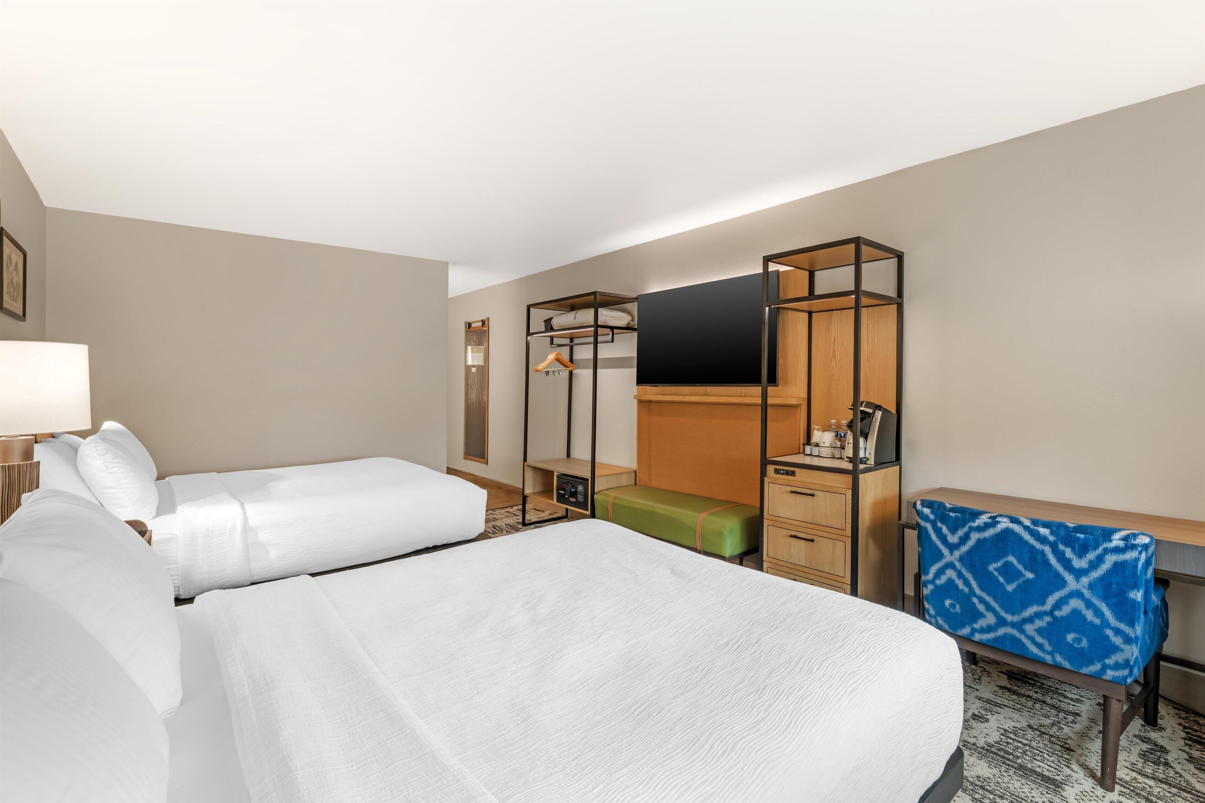 Une chambre d’hôtel avec deux lits, un bureau, une chaise, une télévision et une armoire.