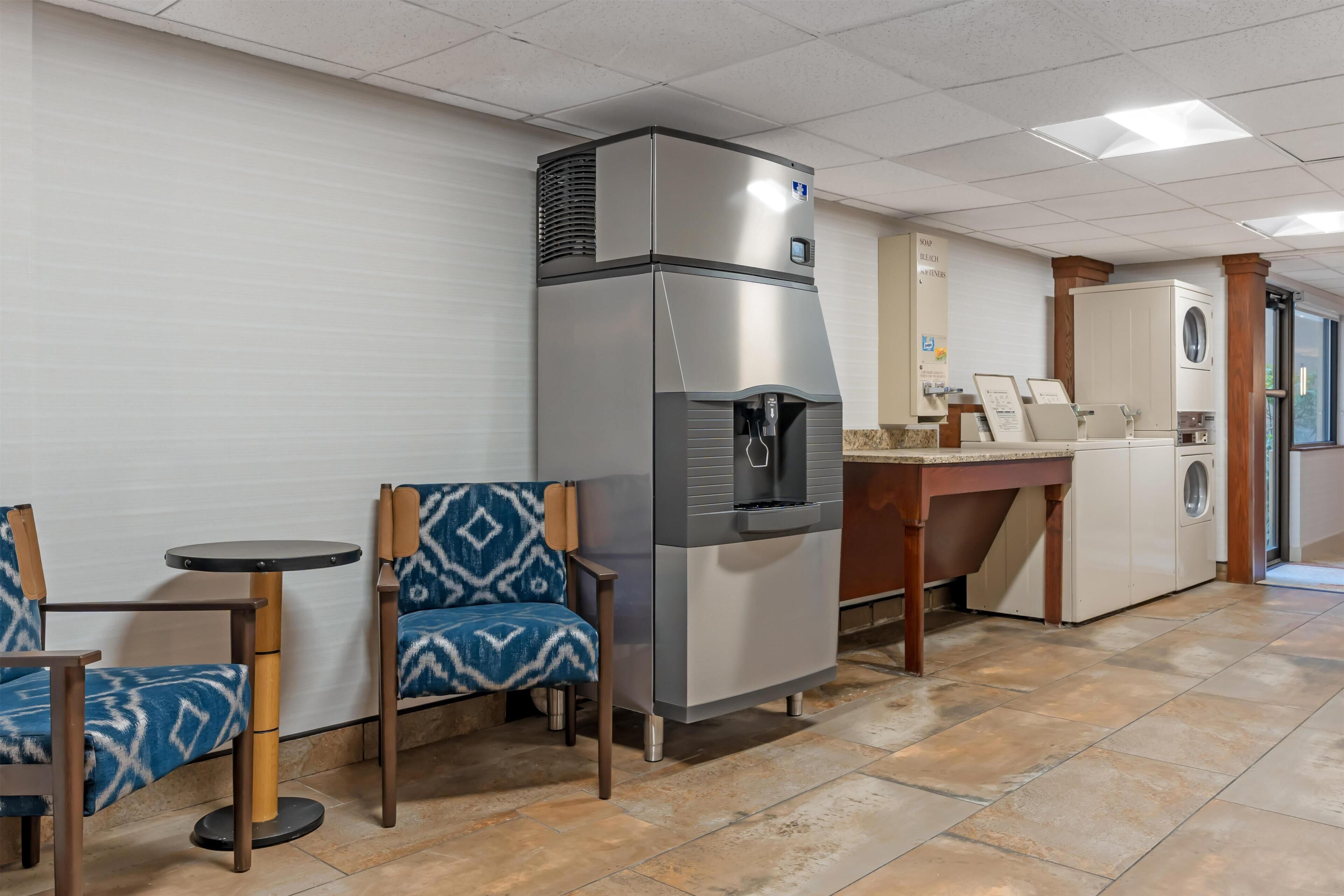 A kitchenette with a refrigerator, microwave, and coffee maker. There are two chairs with patterned cushions and a small round table.