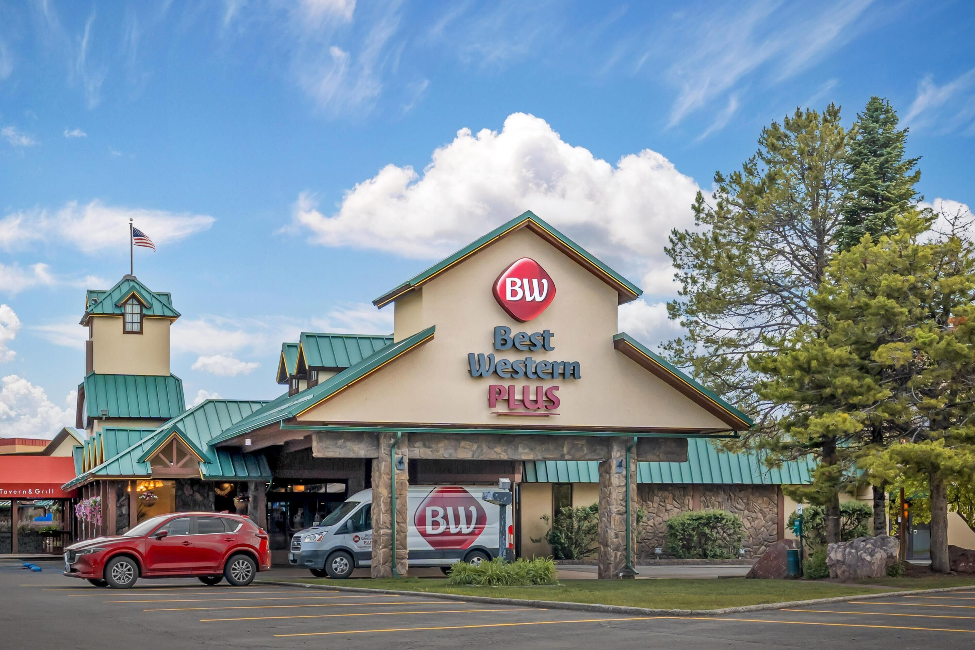 Un hotel Best Western Plus con techo verde, una bandera y un estacionamiento con coches.