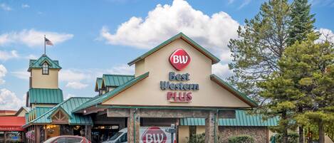 Un hotel Best Western Plus con techo verde, una bandera y un estacionamiento con coches.
