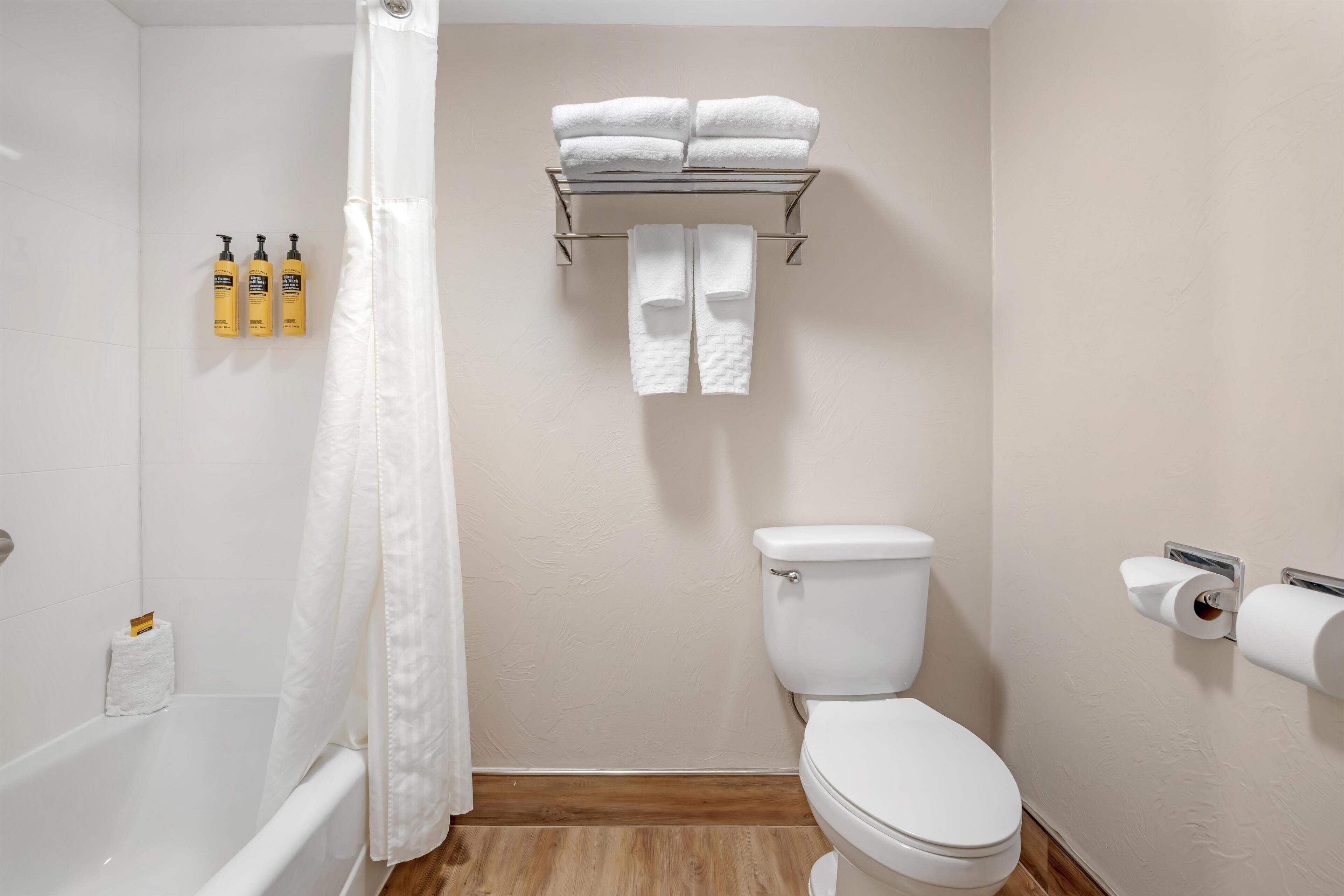 A bathroom with a bathtub, toilet, towel rack, and toiletries.