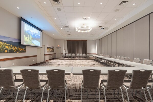 A conference room with a long table, chairs, a projector screen, and a carpeted floor.