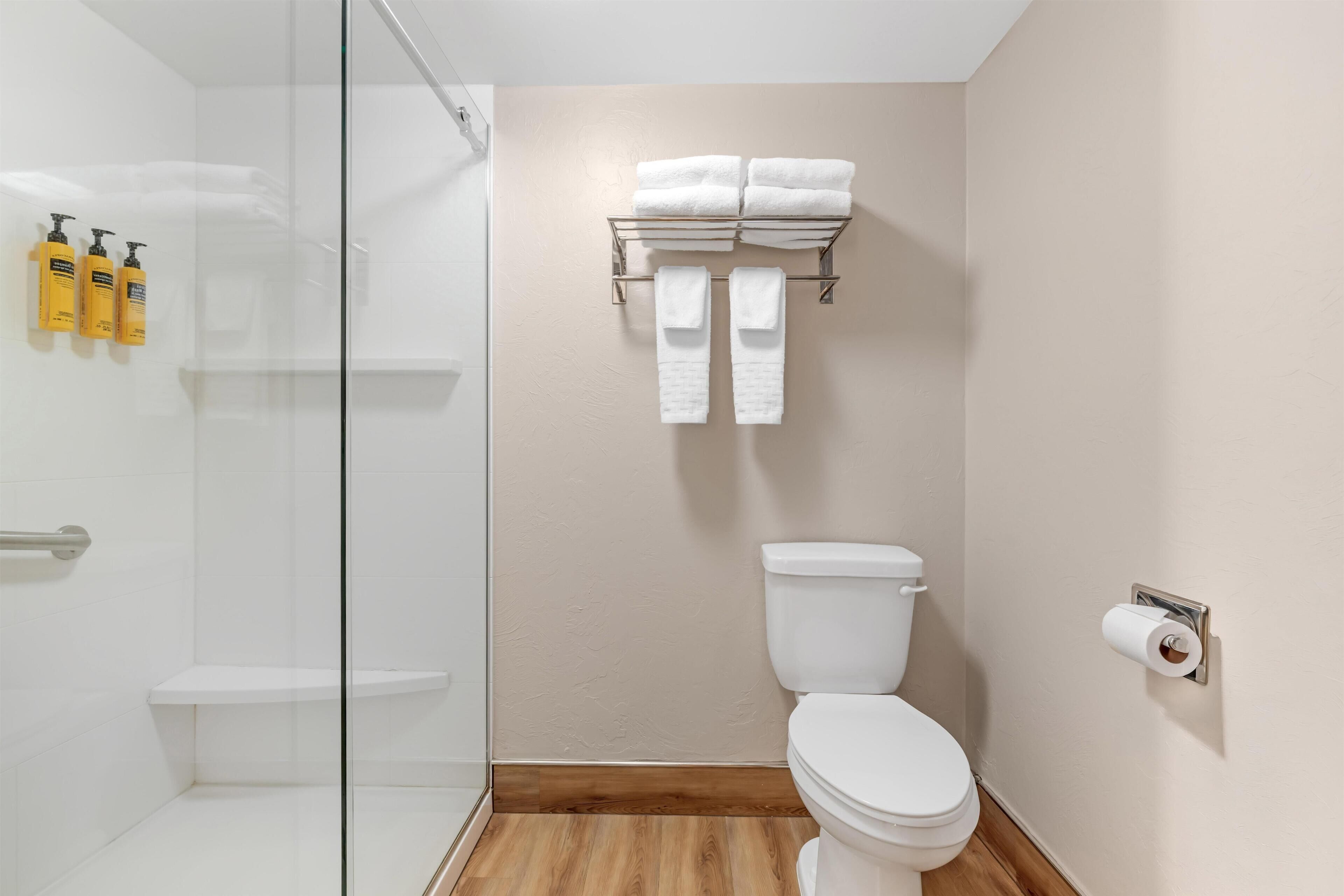A bathroom with a glass shower enclosure, a toilet, a towel rack with towels, and toiletries on the wall.