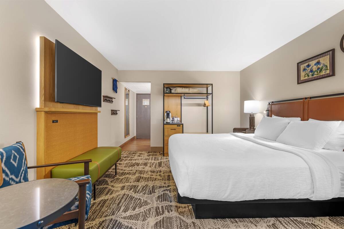 A hotel room with a bed, a TV, a desk, a chair, and a small table.
