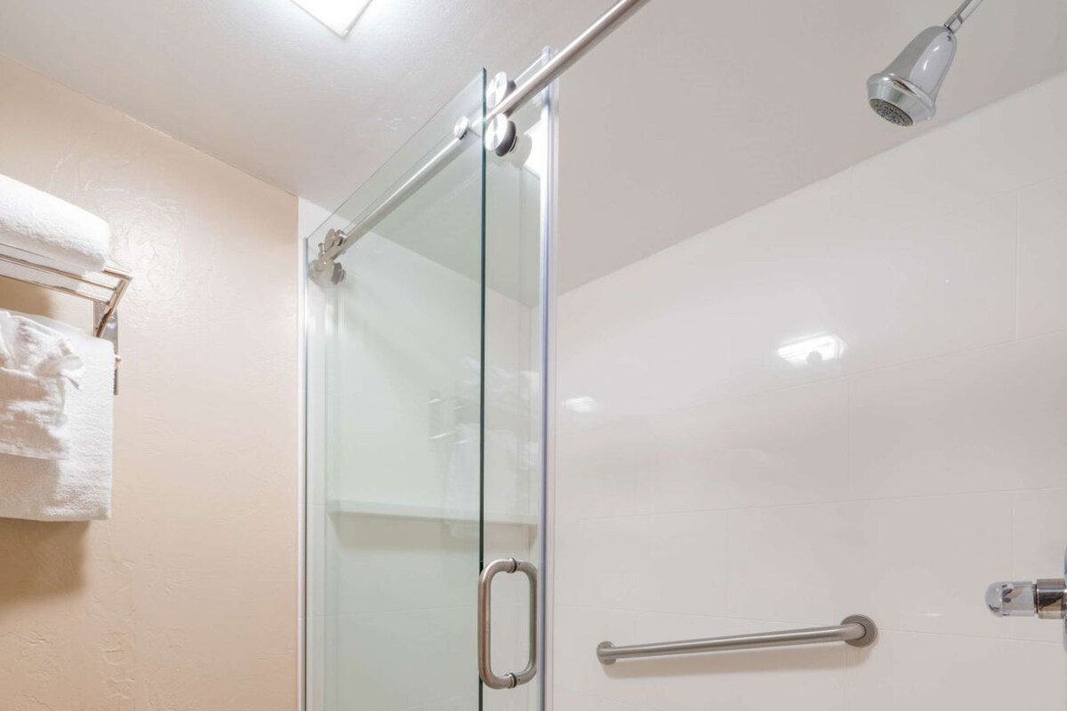 A glass-enclosed shower with a handrail, a towel rack, and a ceiling light.
