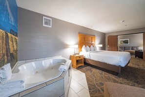 A hotel room with a large bathtub, a bed with a wooden headboard, a nightstand with a lamp, and a painting on the wall.