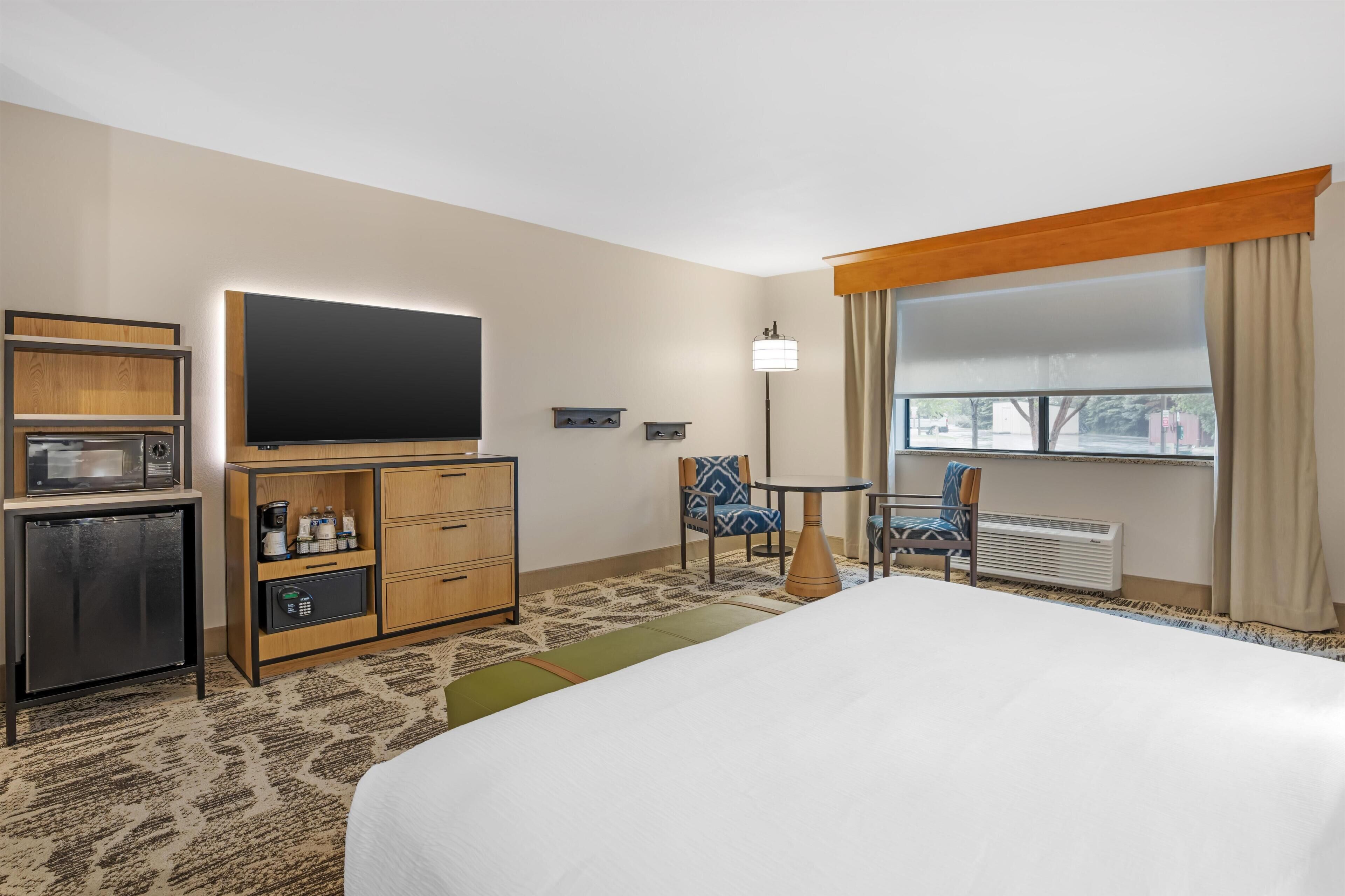 A hotel room with a bed, a TV, a minibar, a desk, and a window with curtains.