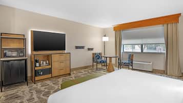 A hotel room with a bed, a TV, a minibar, a desk, and a window with curtains.
