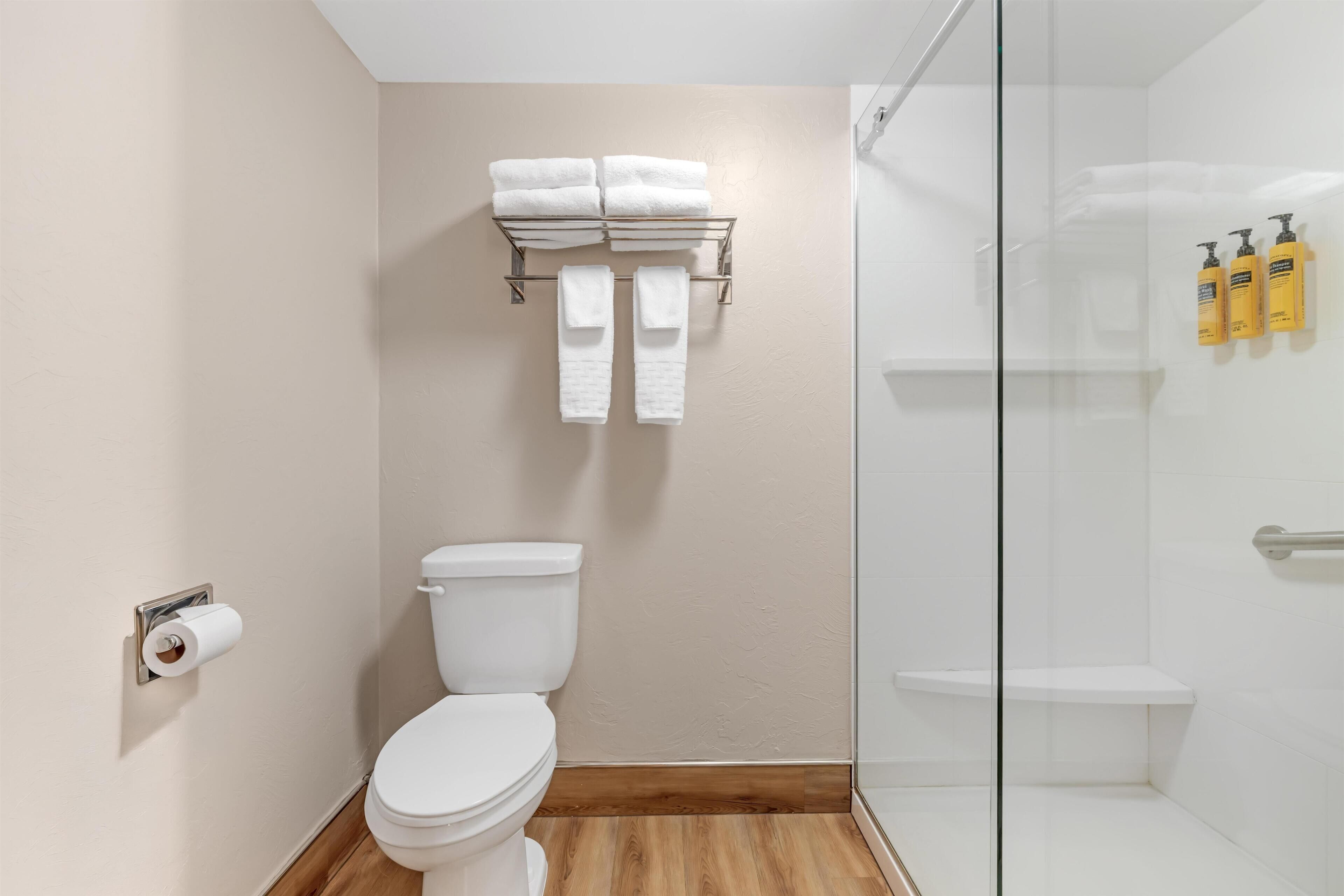 Un baño moderno con inodoro, toallero, cabina de ducha de vidrio y artículos de aseo en la pared.