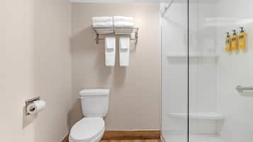Un baño moderno con inodoro, toallero, cabina de ducha de vidrio y artículos de aseo en la pared.