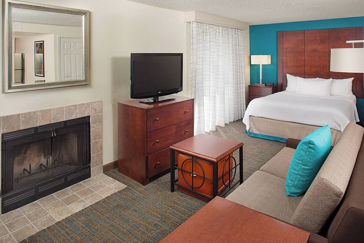 A hotel room with a fireplace, a television, a bed, a nightstand, and a small table.