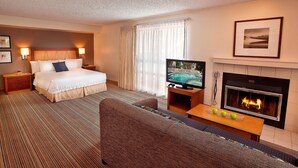 Ett hotellrum med en säng, en soffa, en tv, en öppen spis och ett fönster med gardiner.