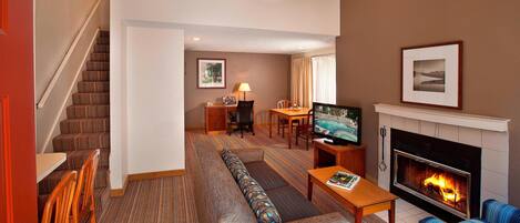 Una habitación de hotel con una escalera, un sofá, un televisor, una chimenea y una zona de comedor.