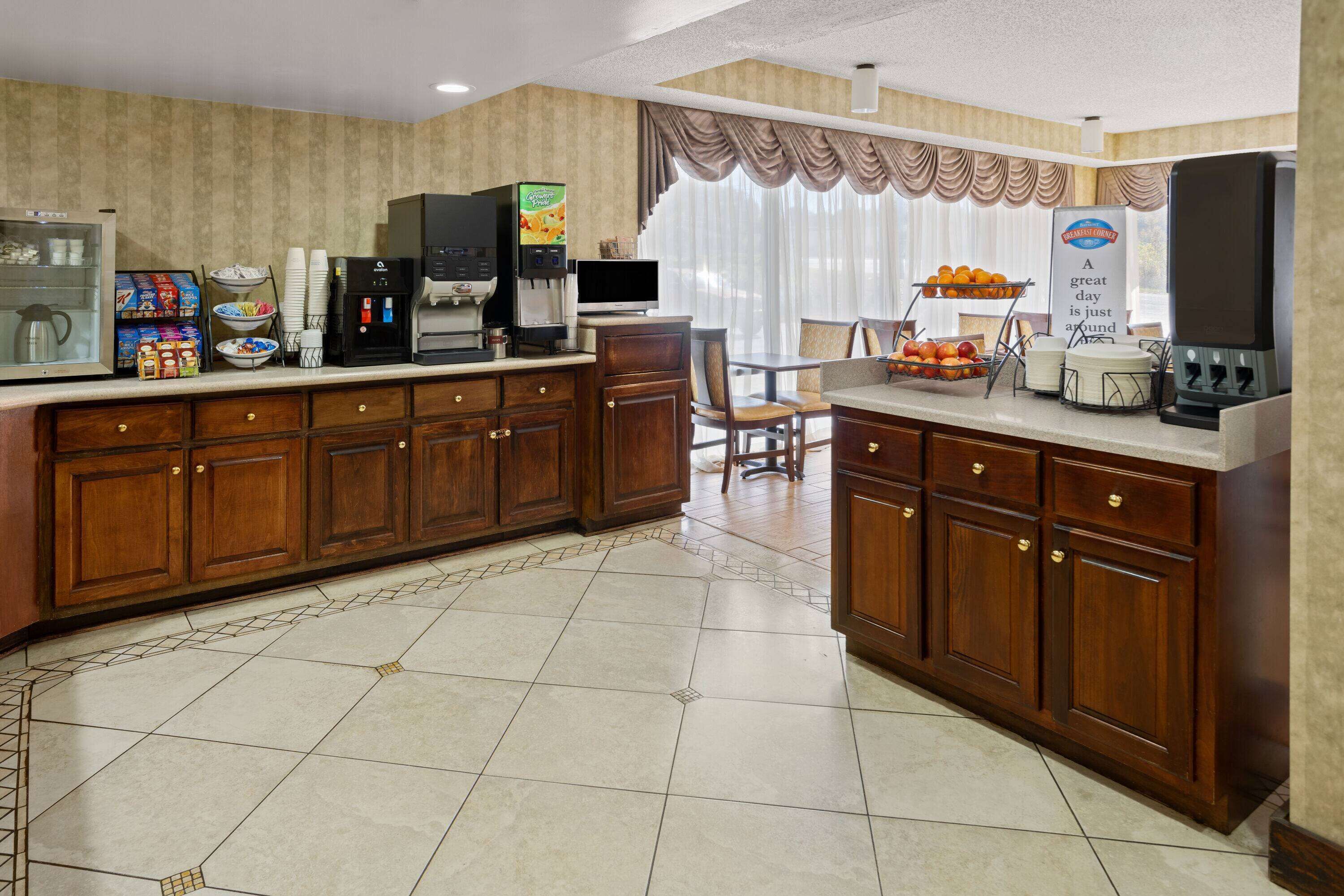 A hotel kitchen with a coffee machine, a fruit display, and a breakfast bar.