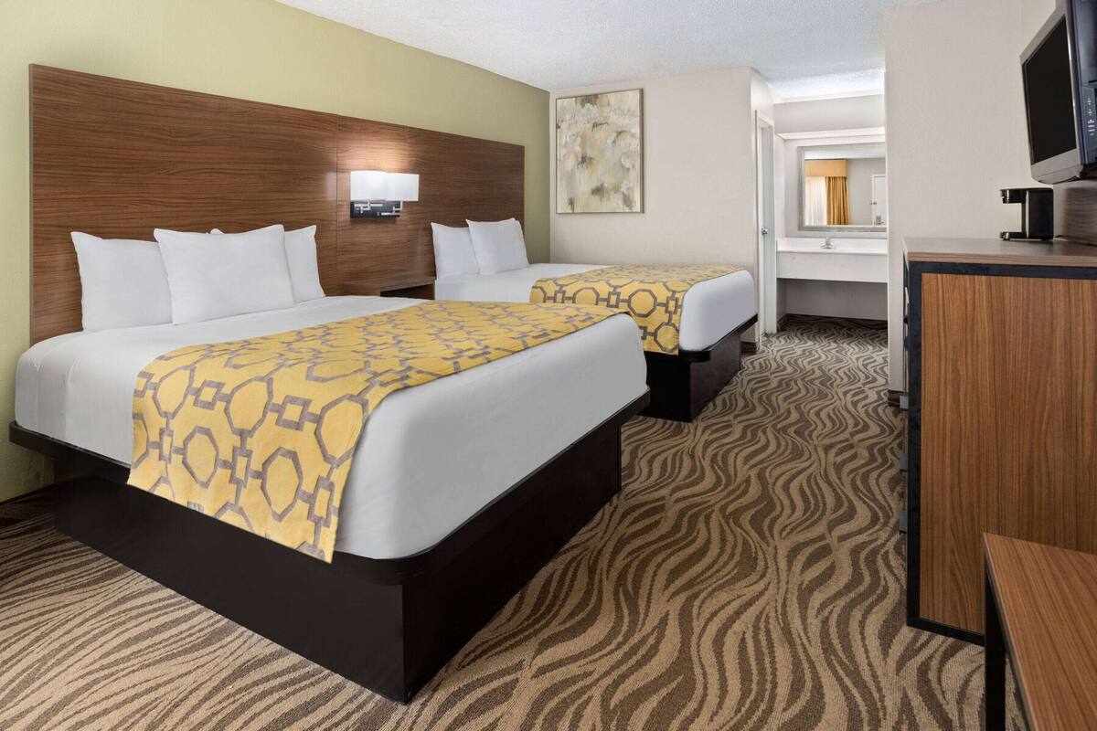 A hotel room with two beds, a TV, a desk, and a bathroom visible in the background.