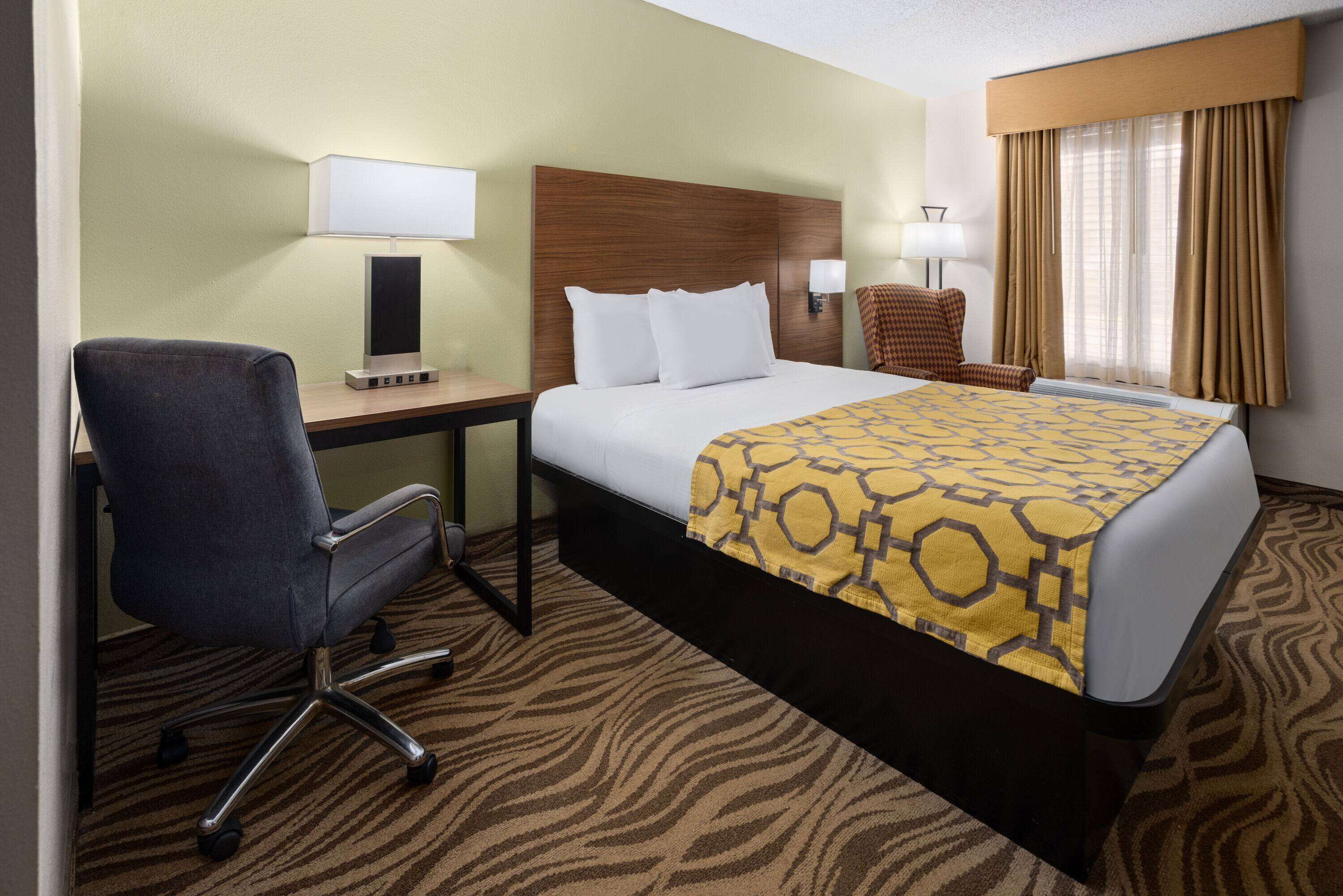 Una habitación de hotel con una cama, un escritorio, una silla y una lámpara.