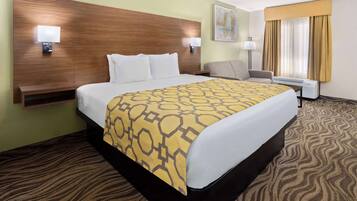 A hotel room with a large bed, a desk, a chair, a nightstand, and a window with curtains.