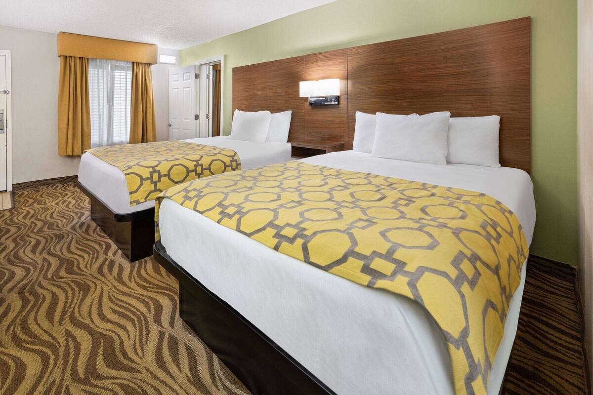 A hotel room with two beds, a wooden headboard, a patterned carpet, and a window with curtains.