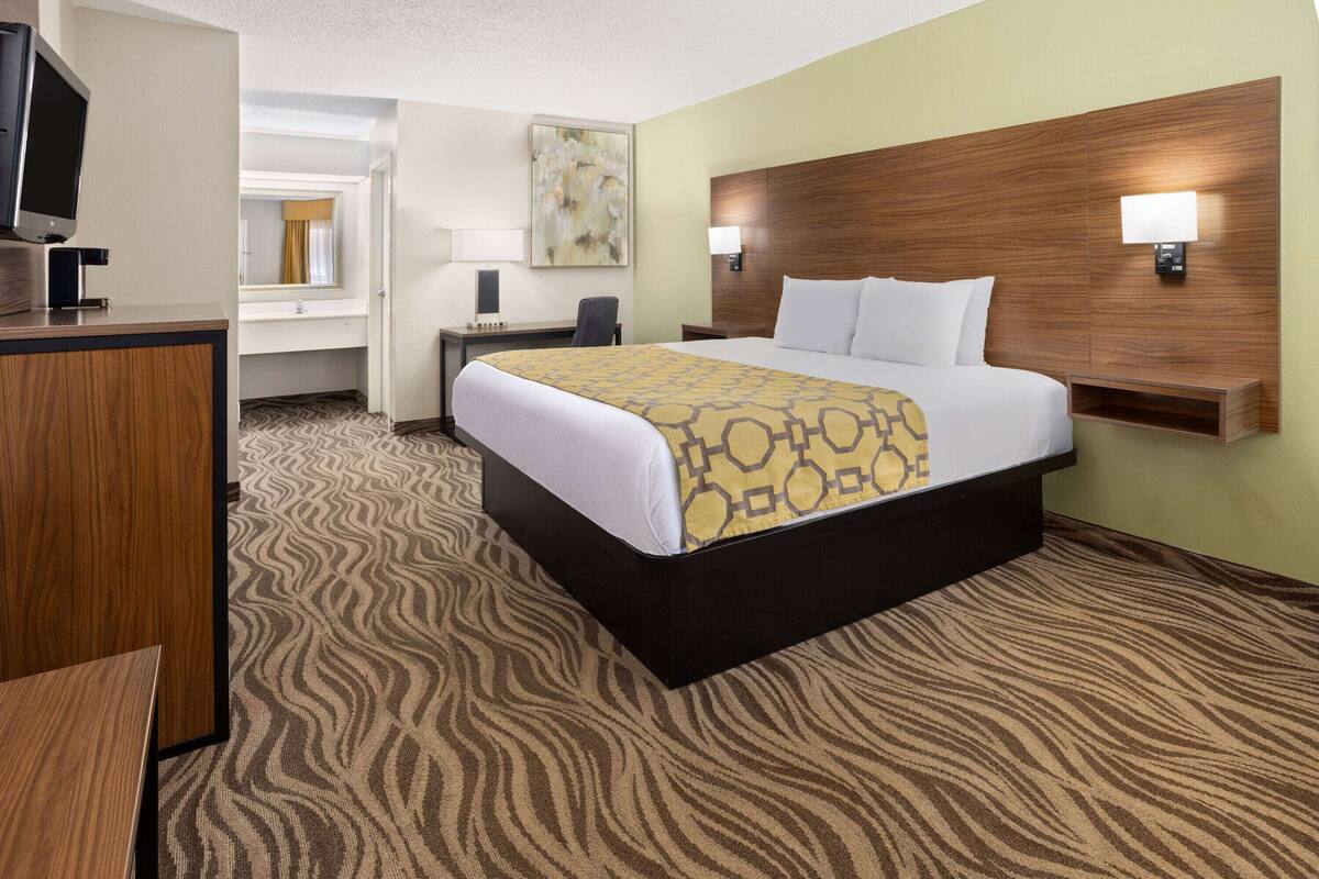 A hotel room with a large bed, a desk, a chair, a television, and a mirror.