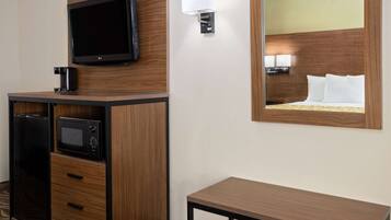 A hotel room with a wooden cabinet, a flat-screen TV, a microwave, a bedside table, and a large mirror reflecting the bed.