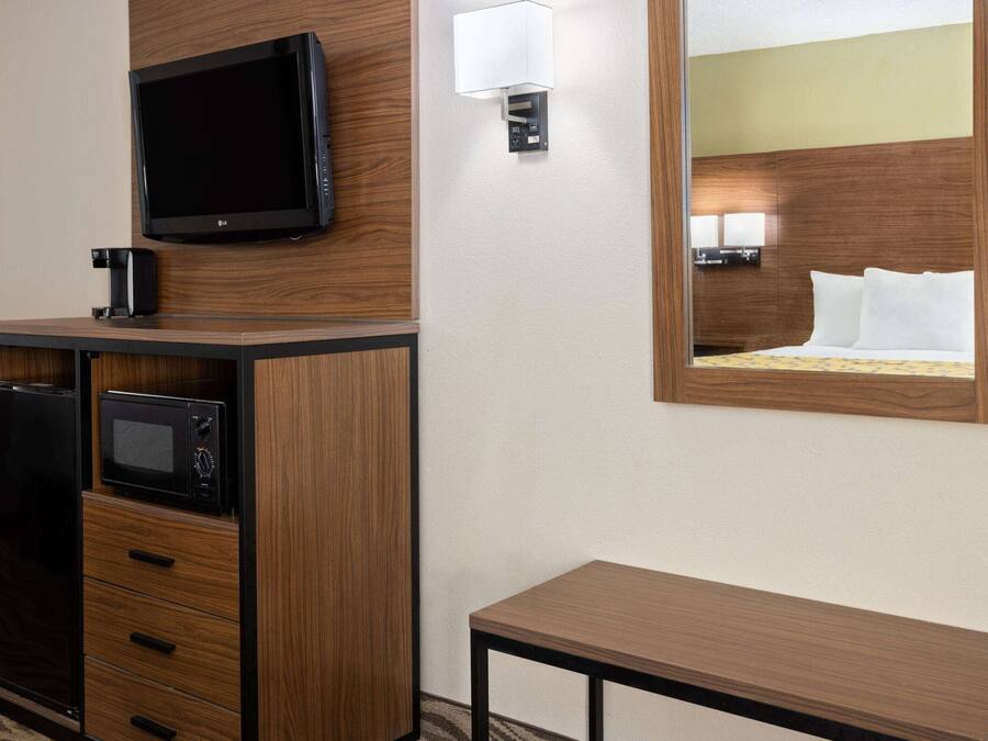 A hotel room with a wooden cabinet, a flat-screen TV, a microwave, a bedside table, and a large mirror reflecting the bed.
