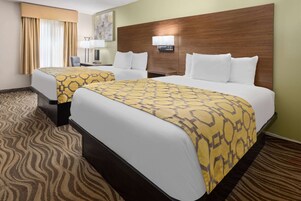 Habitación de hotel con dos camas, cabecera de madera, alfombra estampada y una lámpara en la mesita de noche.