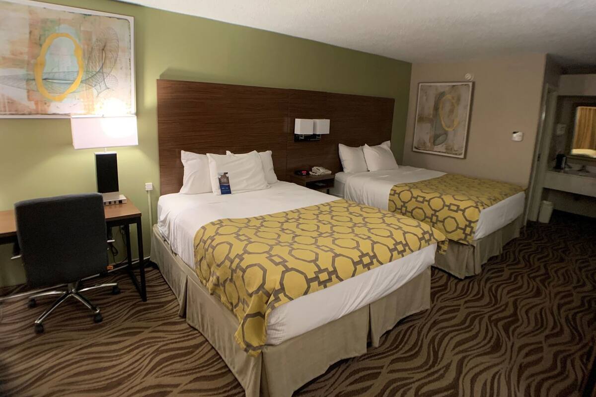 A hotel room with two beds, a desk, a chair, and a large painting on the wall.