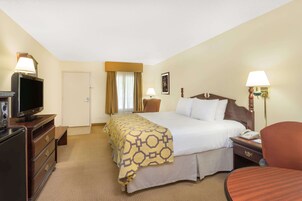 Habitación de hotel con cama, mesita de noche, lámpara, televisión y escritorio con silla.