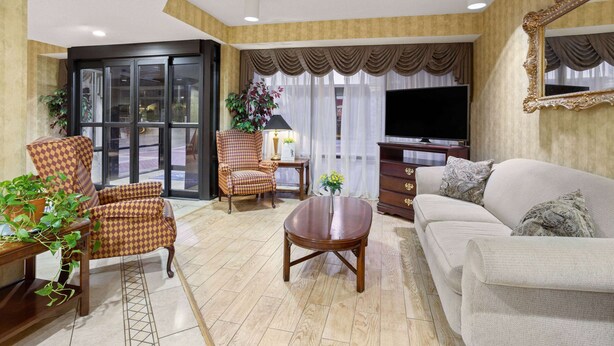 A spacious living room with a sofa, armchairs, a coffee table, and a TV. - Baymont by Wyndham Griffin (Griffin)