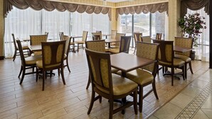 A hotel dining area with multiple tables and chairs, large windows with curtains, and a view of the outside. - Baymont by Wyndham Griffin (Griffin)