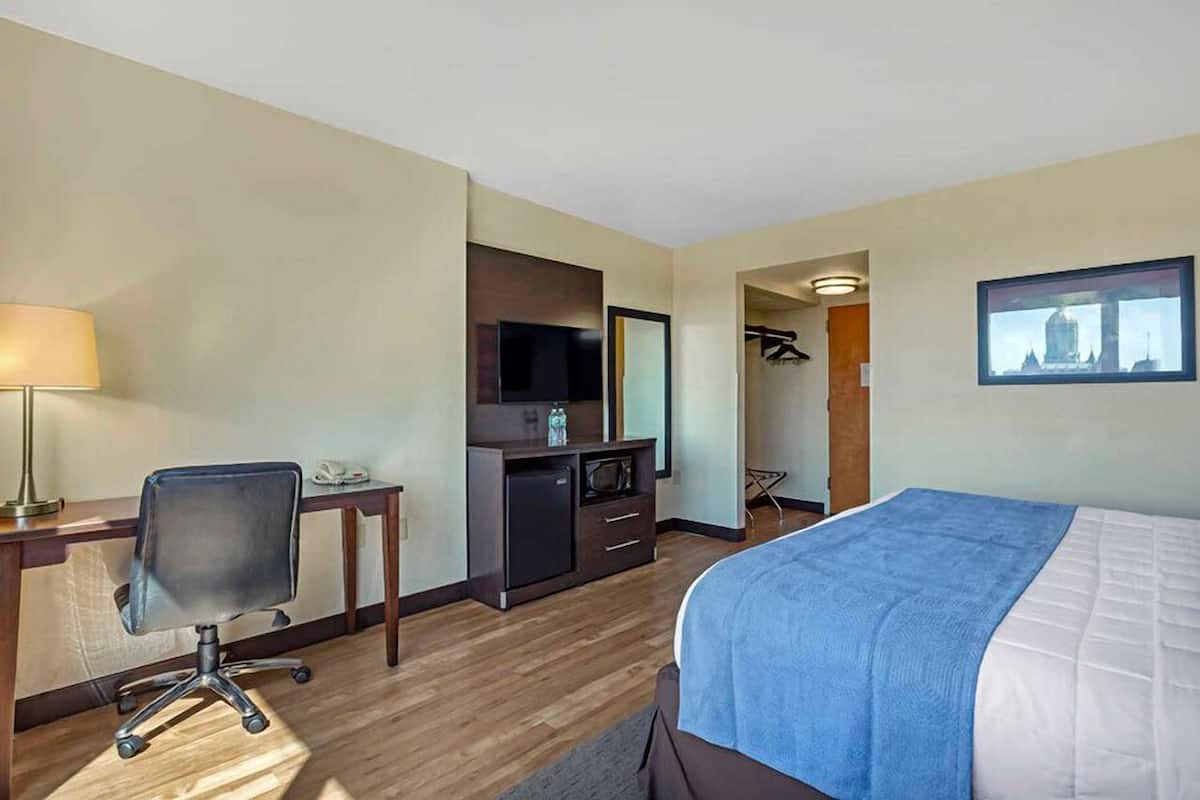 Ein Hotelzimmer mit Bett, Schreibtisch, Stuhl, Fernseher und einer kleinen Küchenzeile.