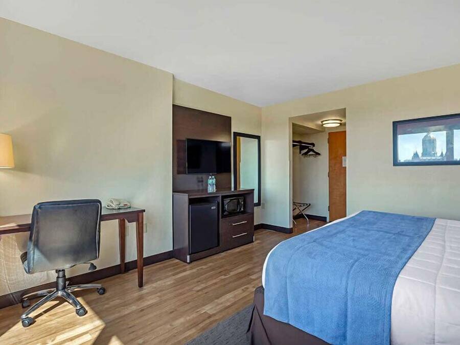 A hotel room with a bed, desk, chair, TV, and a small kitchenette.