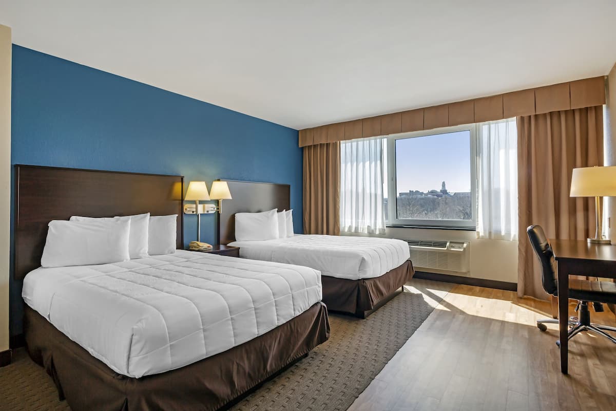 Ein Hotelzimmer mit zwei Betten, einem Schreibtisch und Blick auf eine Stadtlandschaft.