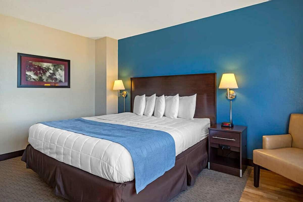 Ein Hotelzimmer mit einem großen Bett, zwei Nachttischen mit Lampen, einem gerahmten Bild an der Wand und einer blauen Akzentwand.