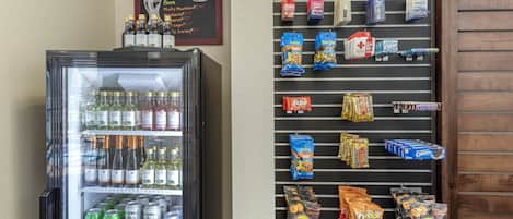 Un refrigerador de bebidas con varias opciones y una pared de aperitivos con diversos bocadillos y refrescos.