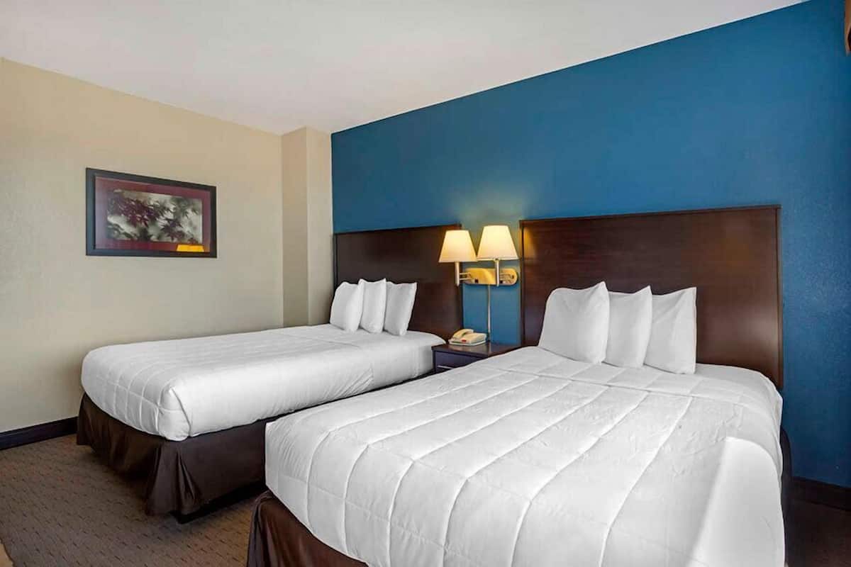 Ein Hotelzimmer mit zwei Betten, einem Nachttisch mit Lampe und einem gerahmten Bild an der Wand.