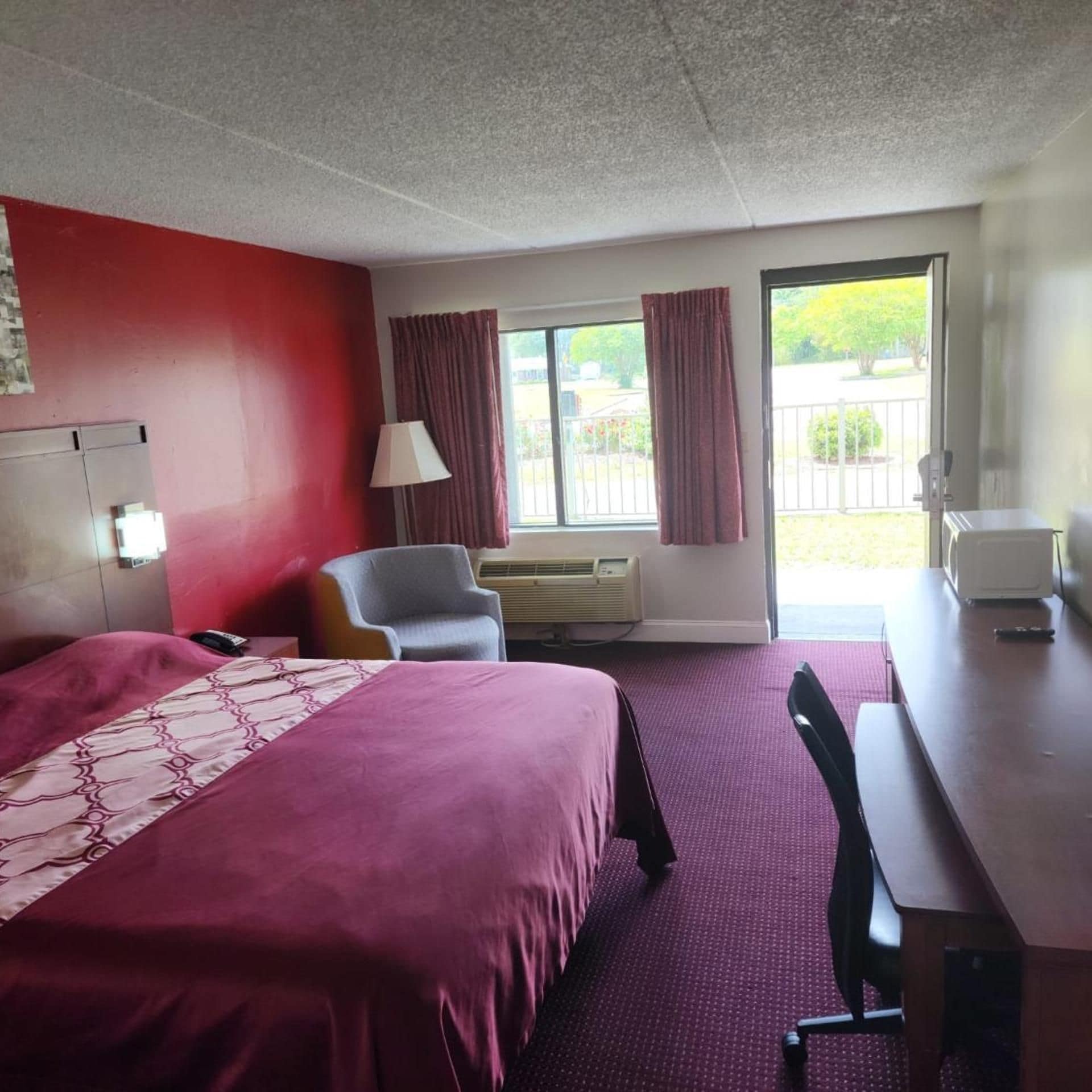 A hotel room with a bed, a desk, a chair, an air conditioning unit, and a window with curtains.