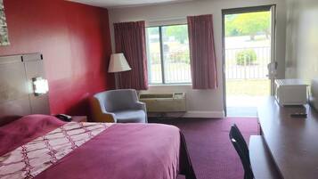A hotel room with a bed, a desk, a chair, an air conditioning unit, and a window with curtains.