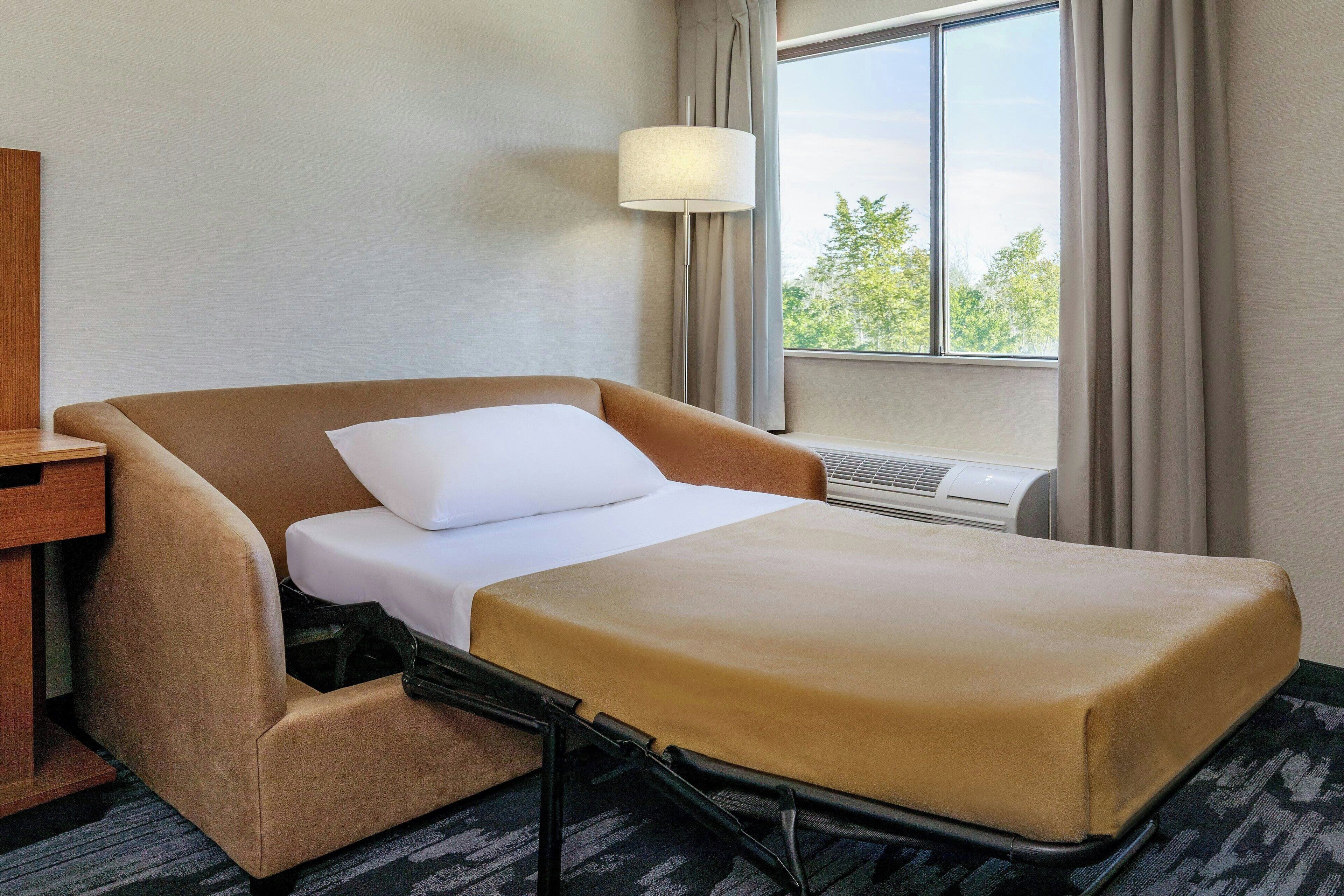 Een hotelkamer met een bed, nachtkastje, lamp en raam met gordijnen.