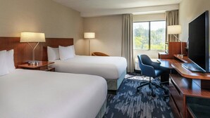 Habitación de hotel con dos camas, un escritorio con ordenador, televisor y ventana con cortinas.